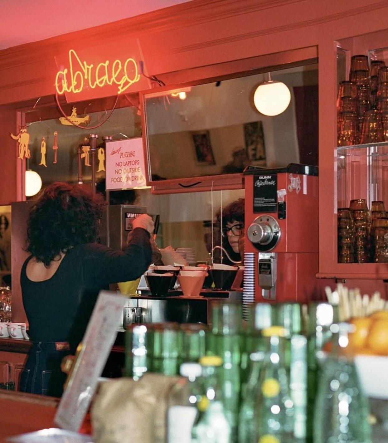 The neon Abraço sign above the counter, with the espresso bar and a barista at work